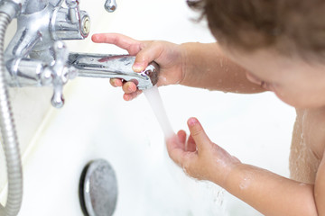 child washes in the bath, baby girl boy plays with a stream of water
