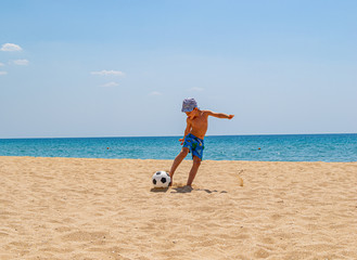 The child plays football on the beach. The concept of sport and healthy lifestyle.Fresh sea air and good ecology. Copy space.