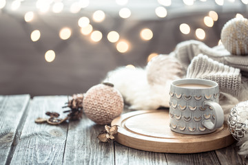 Coffee cup over Christmas lights bokeh in home on wooden table with sweater on a background and decorations. Holiday decoration, magic Christmas