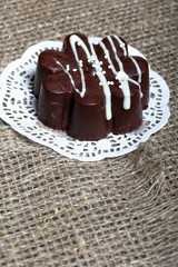 Chocolate dessert in the shape of a flower. Dark chocolate coated. Garnished with white chocolate and sprinkles. On coarse linen cloth.
