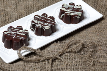 Chocolate dessert in the shape of a flower. Dark chocolate coated. Garnished with white chocolate and sprinkles. On coarse linen cloth.