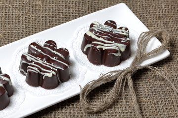 Chocolate dessert in the shape of a flower. Dark chocolate coated. Garnished with white chocolate and sprinkles. On coarse linen cloth.