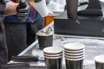 Seller of Ice Cream adding Topping as chocolate Syrup on sweet Dessert in paper Cup in Street Cafe