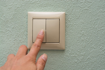 finger presses an electronic light switch on a blue wall background