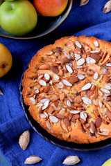 Pie with pears, apples and almonds on a black ceramic plate surrounded by the ingredients
