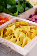 Yellow pasta farfalle in a wooden box. Multicolored pasta in the background