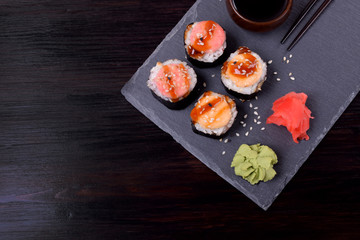 Sushi rolls assortment, wasabi, marinated ginger and soy sauce served on slate plate on black table