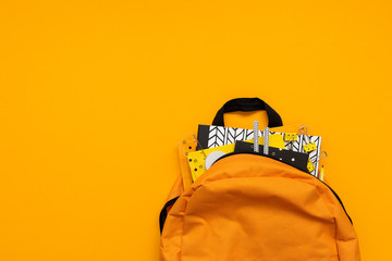 Back to school concept. Backpack with school supplies on yellow background. Top view. Copy space. Flat lay