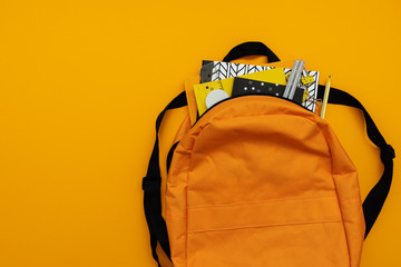 Back to school concept. Backpack with school supplies on yellow background. Top view. Copy space....