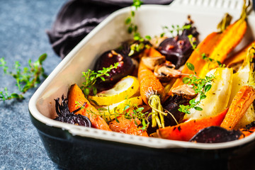 Baked vegetables with thyme in the oven dish, blue background.
