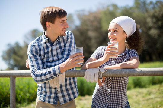 country couple of farmers drink milk in field near fenc