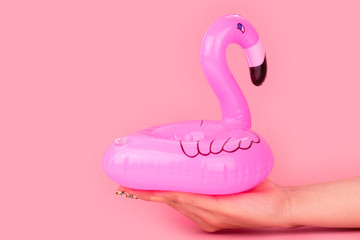 Mini pink flamingo in woman's hands isolated on pink background. Summer beach composition. Flat lay, copy space.