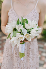 Bride Hold in Hand Tulip Wedding Bouquet Outside. Detailed Shot of Woman with Bunch of White Flowers Decorated with Satin Ribbon. Outdoor Marriage Ceremony Detail Shallow Focus. Summer Event