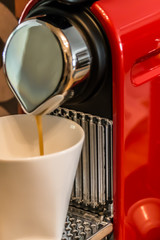 Making coffee: close-up of a red cup-based coffee machine, pouring coffee in a white mug