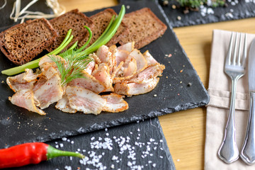 sliced ​​bacon on black slate with bread and onions