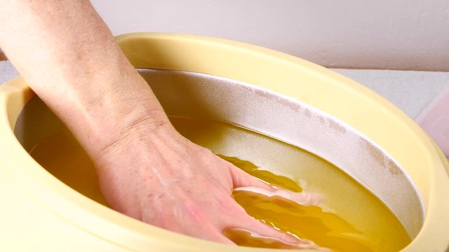 Close up slow motion shot of unrecognizable woman putting hand into paraffin bath taking care of hands skin