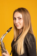 Beautiful european girl holds saxophone on yellow background