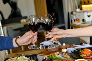 glasses with red wine in hands toasting against the backdrop of the restaurant