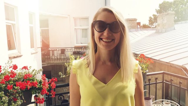 happy smiling attractive woman with sunglasses on sunny romantic balcony with flower boxes
