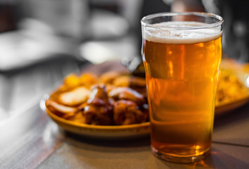 glass of cold beer and plate with snacks on wooden table background on bar or pub