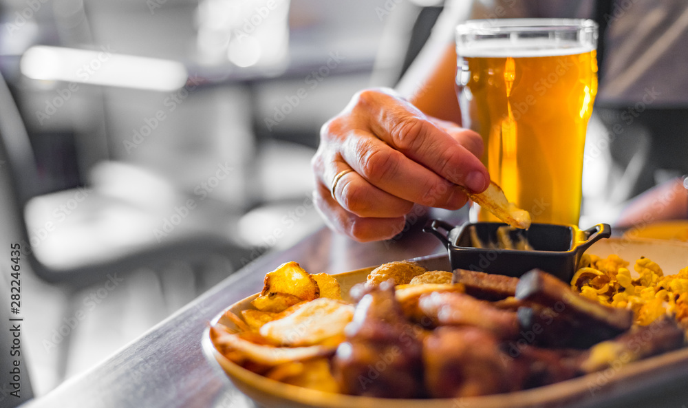 Wall mural man hand with glass of cold beer and plate with snacks on wooden table background on bar or pub