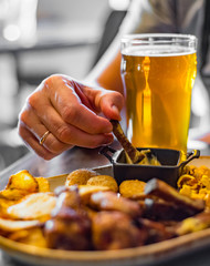 man hand with glass of cold beer and plate with snacks on wooden table background on bar or pub