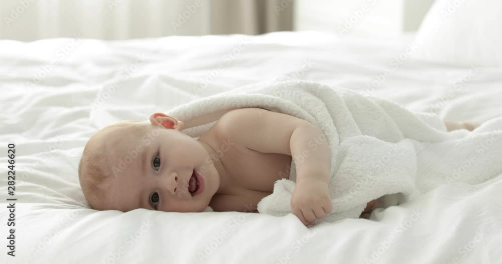 Sticker Adorable little child with towel after bathing on bed at home