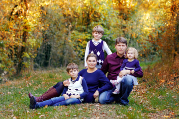 Naklejka na ściany i meble Portrait of young parents with three children. Mother, father, two kids brothers boys and little cute toddler sister girl having fun together in autumn forest. Happy family of five
