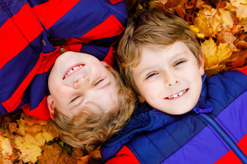 Two little kid boys lying in autumn leaves in colorful fashion fall clothing. Happy healthy...