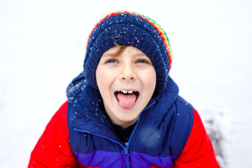 Portrait of little school kid boy in colorful clothes playing outdoors during snowfall. Active leisure with children in winter on cold snowy days. Happy healthy child having fun and playing with snow.