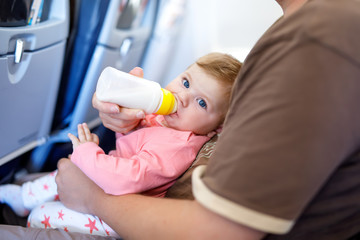 Father holding his baby daughter during flight on airplane going on vacations