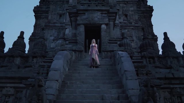 Dramatic portrait. Woman in long dress stay with no move at old ruins, Prambanan temple in Java island, handled static shot