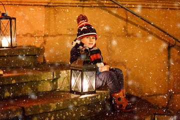 Little cute kid boy with with a light lantern on stairs near church. Happy child on Christmas...