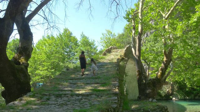 family walks along the old stone bridge. Sights. Konitsa bridge and Aoos River, Greece.