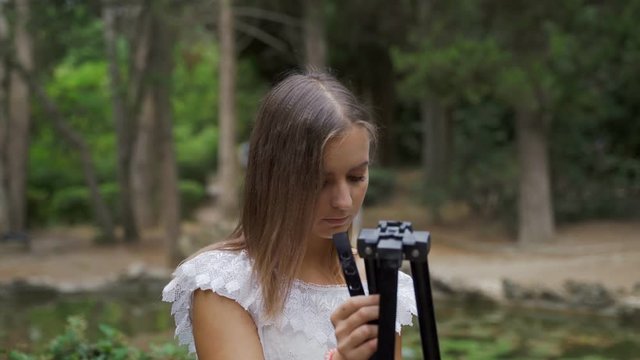 Girl artist prepares paper palette and paint brushes for landscape painting in the park with a small pond 4k