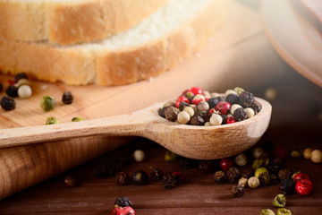 Set of black, pink, white and green pepper corns in wooden spoon on bamboo board and sliced toast bread. Mixed colorful peppercorns spieces.