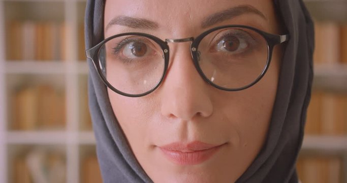 Closeup portrait of young arabian female face in glasses and hijab looking at camera smiling cheerfully in library indoors