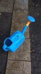 Blue garden watering can stands on a gray path