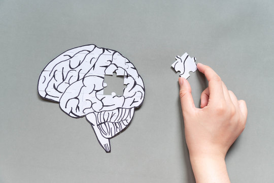 Female hand trying to connect a missing jigsaw puzzle of human brain on gray background. Creative idea for solving problem, memory loss, dementia or Alzheimer's disease concept. Mental health care.