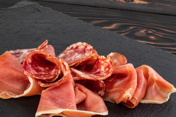 Italian prosciutto crudo or spanish jamon and sausages. Raw ham on stone cutting board
