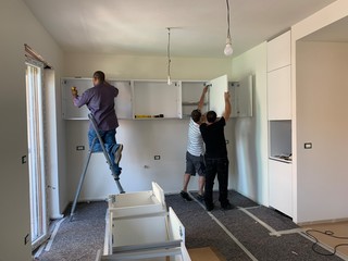 Carpenters installing cabinets and counter top in a white kitchen. Partially installed furniture.