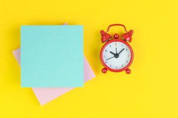 Stack of sticky notes with read alarm clock on solid yellow background with pink and blue on top...