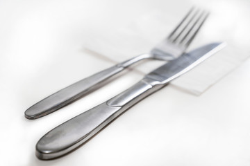 On a white table and white napkin are a knife and a fork.