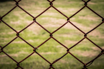 The close up of brown wire fence (barricade) which is hardly rusted in blurred background (meadow).