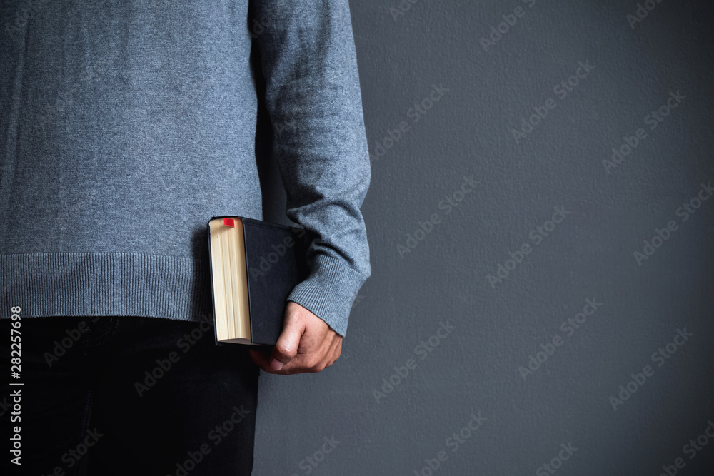 Wall mural a young man is holding a black bible.christians and bible study concept.copy space