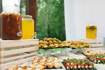 Glass jars of lemonade on wedding candy bar. Catering. Drinks on wedding party. Summer wedding in the forest. Elegant wedding table arrangement