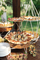 Tasty meals and sandwitches on a brown rustic wooden banquet table. Summer wedding in the forest. - 282257652