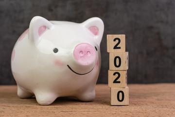 Year 2020 financial goal, savings, budget or investment, happy smiling pink piggy bank with stack of wooden cube blocks with number 2020 on table and dark black background