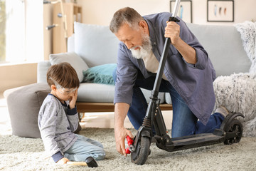 Cute little boy with grandfather repairing kick scooter at home © Pixel-Shot