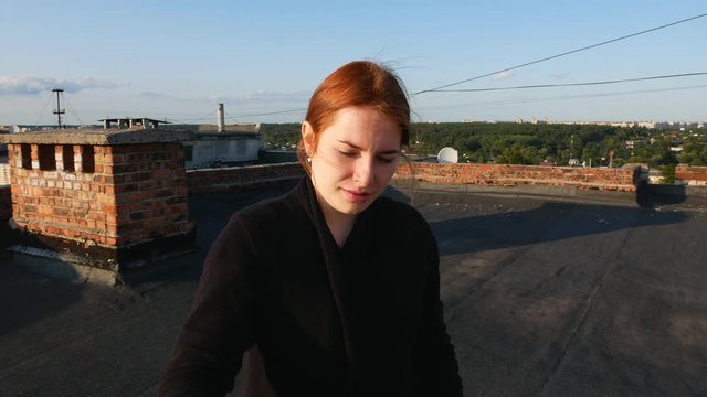Red-haired girl paints a picture. On the roof of the house on a sunny day.